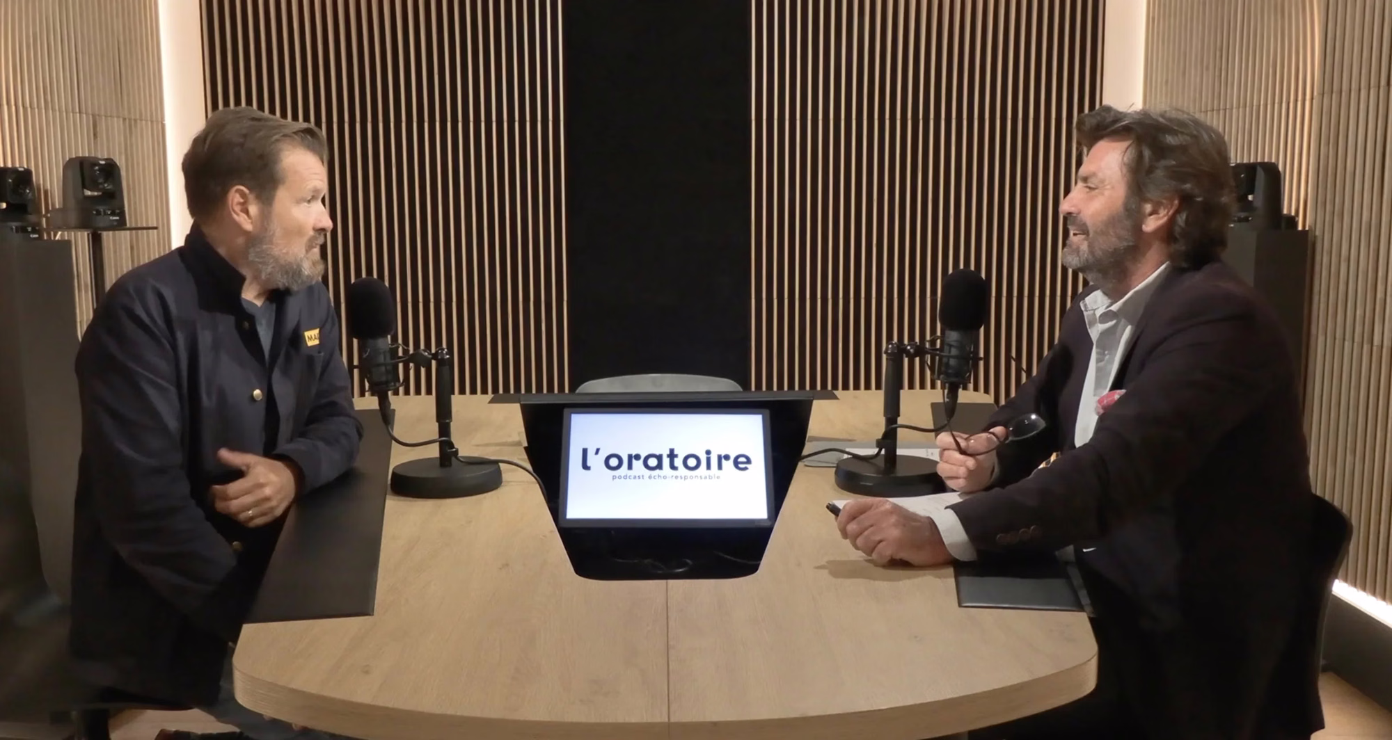 Two speakers at the mic around the studio desk during a company podcast recording